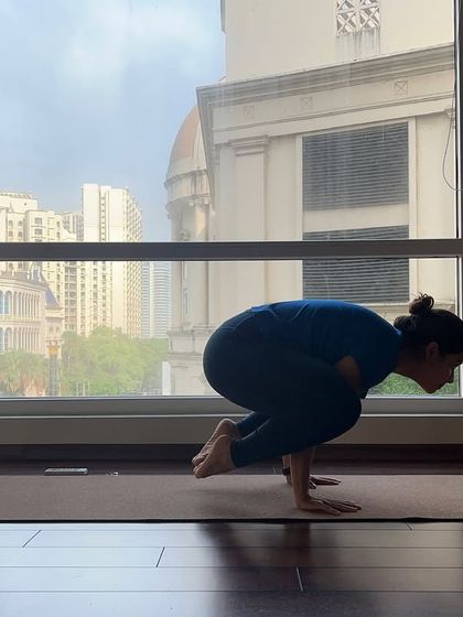 The silhouette of a student practicing Bakasana (Crow Pose) against the window, finding balance as the city moves outside.