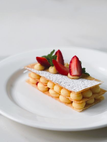A classic strawberry Mille-feuille, featuring layers of crisp puff pastry, creamy crème pâtissière, and fresh Mahabaleshwar strawberries. A truly elegant dessert.