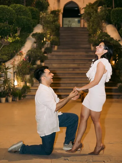 The classic proposal moment, with the groom on one knee, and the bride's reaction of pure joy and surprise.