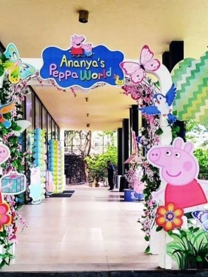 A cheerful entrance for "Ananya's Peppa World" party. The archway is decorated with cutouts of Peppa Pig characters, flowers, and trees.