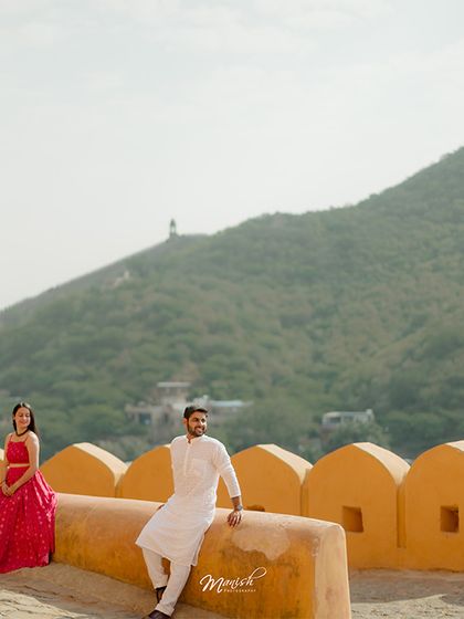 A wide-angle shot capturing the scale of the fort and the beautiful landscape, with the couple as the romantic centerpiece.