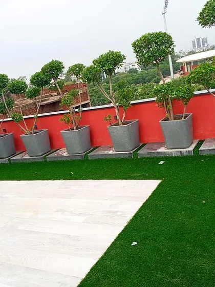 A row of neatly trimmed topiary trees in grey planters lines this rooftop space. The design combines a pristine artificial lawn with a light-colored tile patio area, creating a clean and organized look.