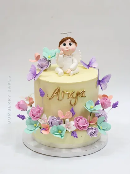 A lovely baptism cake for little Anya, featuring a sweet angel figurine, pastel flowers, and delicate butterflies.