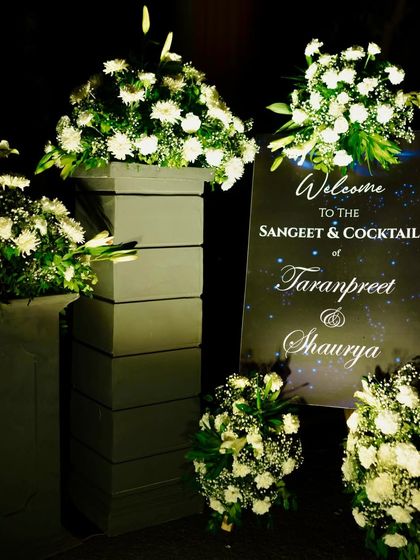 The welcome signage for the Sangeet & Cocktail night, elegantly designed and surrounded by lush arrangements of white flowers.