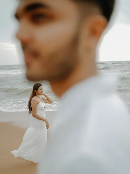 An artistic shot on a Goa beach, with the groom out of focus in the foreground. This composition draws the eye to the bride and the sea, creating a dreamy and contemplative mood.