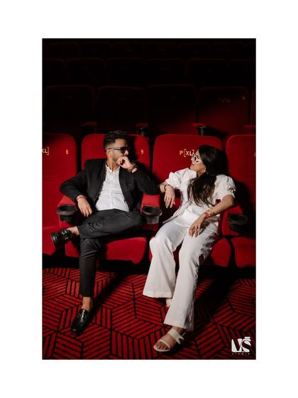 A stylish, editorial-style portrait of a couple in theatre seats. Their confident poses and the bold red and black color scheme create a modern and high-fashion look.