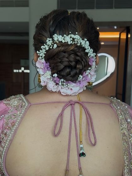 A lovely bridal bun created with a mix of baby's breath and light purple flowers. This style is perfect for a daytime wedding or a bride looking for a soft, romantic floral arrangement in her hair.