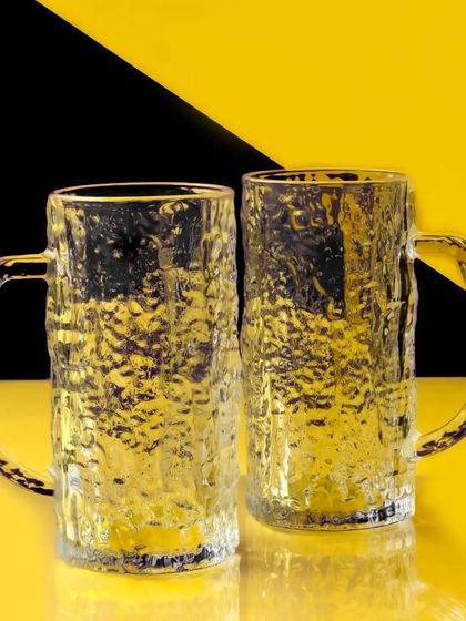 Two empty beer mugs are shot against a bold, graphic background of yellow and black. This modern, high-contrast approach creates a visually striking and edgy product photo.