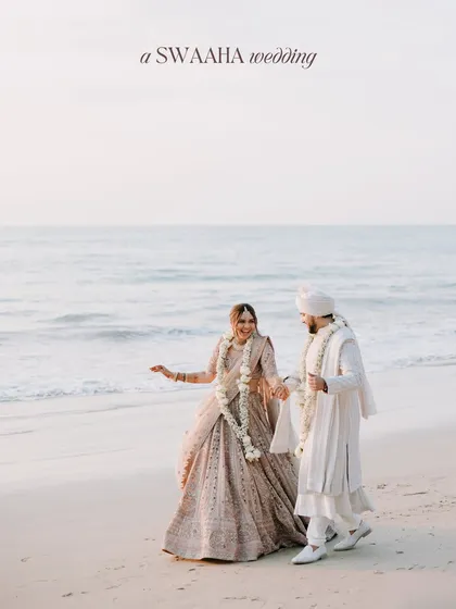 A serene portrait of the couple walking hand-in-hand on the beach after their ceremony, dressed in elegant white and pastel attire.