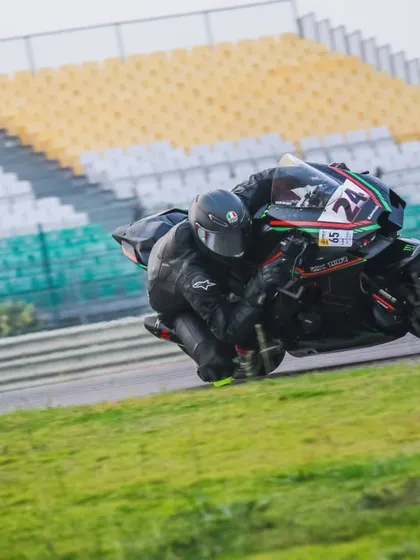 A rider leans into a corner with the iconic grandstands of the Buddh International Circuit in the background. A truly world-class experience.