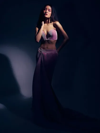 A study in mood and color. The model is bathed in a dramatic, shadowy light, with the pink, shell-like top and flowing skirt creating a mermaid-esque, ethereal silhouette.