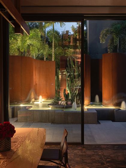 A view from the dining area of the KEUS office, looking out onto the illuminated water feature at dusk. The design seamlessly connects the interior space with the dynamic outdoor landscape.