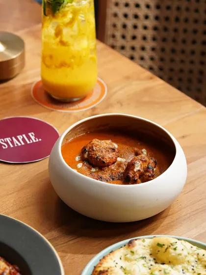 A comforting bowl of butter chicken paired with a bright summer cooler. This image balances a classic Indian dish with a modern beverage, showing the restaurant's range.