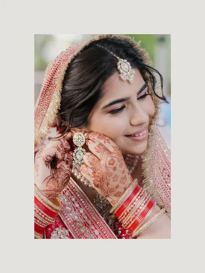 A candid moment of the bride adjusting her earring, her hands adorned with beautiful mehndi. We love capturing these small, natural gestures that happen while getting ready.