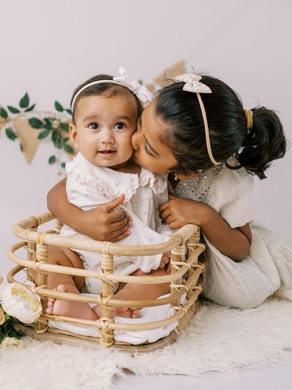 A sweet moment between sisters. The older sister gives her baby sister a gentle kiss during a half-birthday celebration.