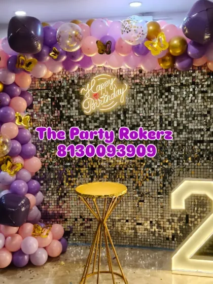 A beautiful setup for a 22nd birthday, featuring a silver sequin wall, a purple and pink balloon arch with butterfly accents, and a marquee number.