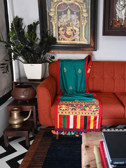 The throw draped over a modern orange sofa, demonstrating its ability to bridge different decor styles. The rich green silk and vibrant embroidery create a stunning focal point.