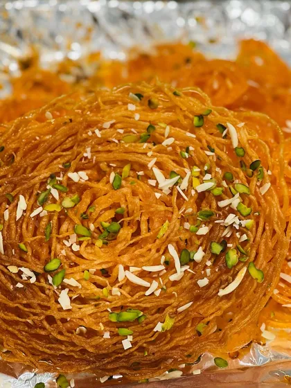 For those looking for something beyond the ordinary, we offer specialty sweets like this intricate Ghevar. It's a crispy, delicate dessert, garnished with nuts, that adds a wow factor to any festive occasion.