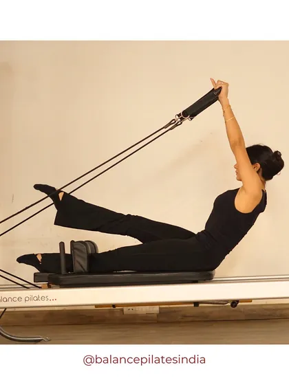 A client performs a teaser variation with feet in straps on the reformer. This move deeply engages the core while also working the legs and arms.