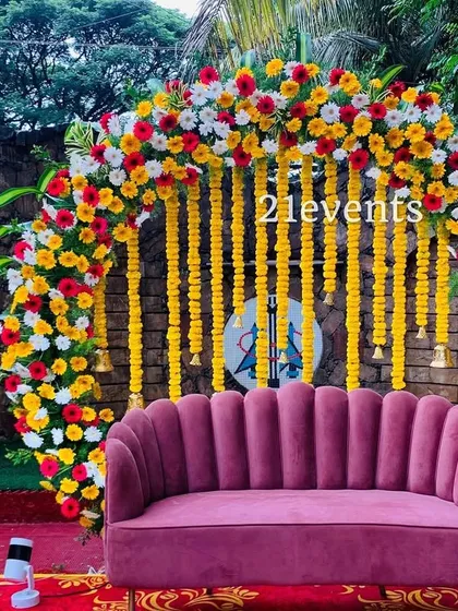 A bright and cheerful outdoor setup for a pre-wedding event. The circular arch is heavily decorated with yellow, red, and white flowers, complemented by hanging marigold strings.