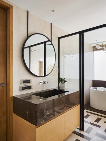 The master bathroom in this Mumbai duplex features a dark marble vanity and a round mirror suspended by black straps. The patterned floor tiles add a graphic element to the otherwise serene space.