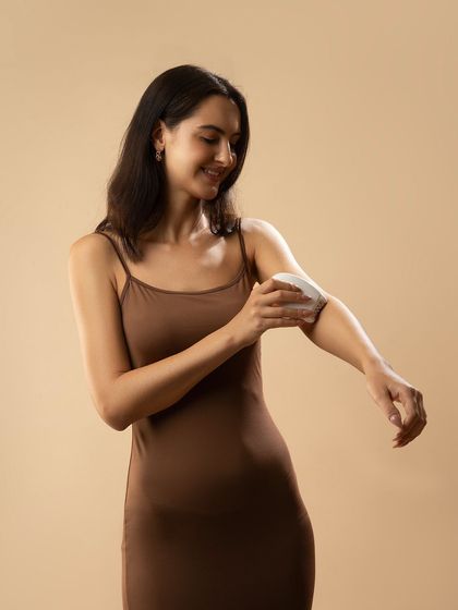 A model applying a product from a small epilator. The soft, neutral background and her gentle expression create a calm and pleasant mood.