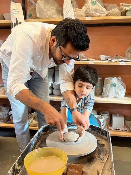 A father gently guides his son's hands on the potter's wheel. Our family workshops are designed to be a bonding experience, creating a space for connection and shared creativity.