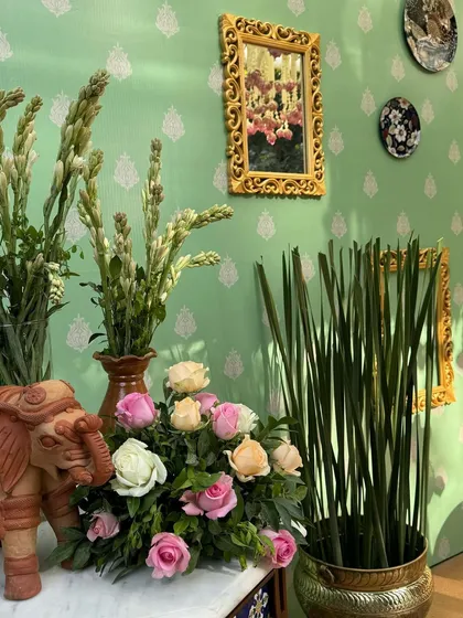 A close-up of the decor, featuring a terracotta elephant, brass pots, and pastel roses against the custom-printed green wall.