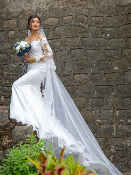 A stunning full-length bridal portrait showcasing the bride's gorgeous gown and long, flowing veil against a rustic stone wall.