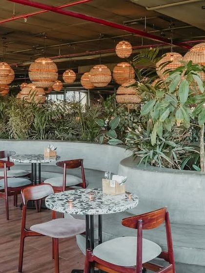 The design incorporates large, curved concrete planters to divide the space and bring in abundant greenery. This biophilic element softens the industrial feel and creates a refreshing, garden-like atmosphere.