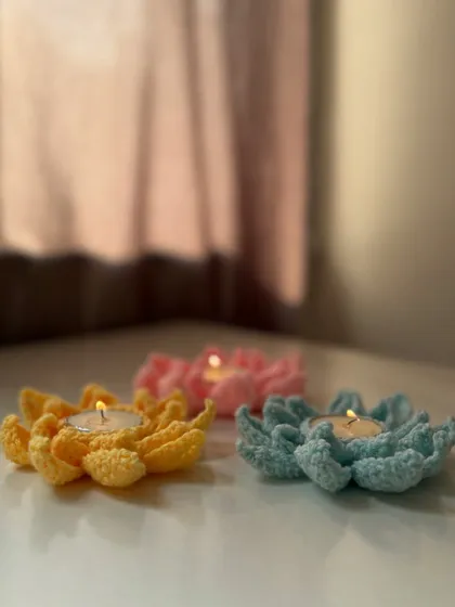 Three colorful crochet lotus tea light holders glowing on a table, adding warmth and elegance to any festive celebration.