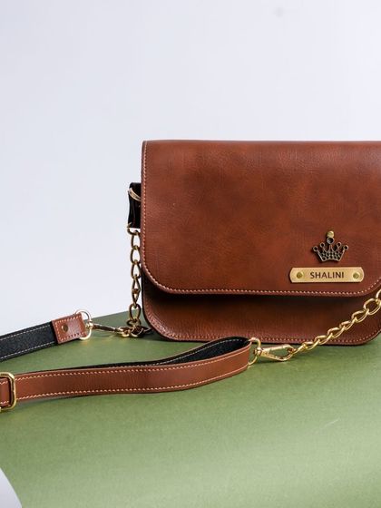 A detailed look at the tan NEXON sling bag, customized with a name and a crown charm. It comes with an adjustable premium chain strap.