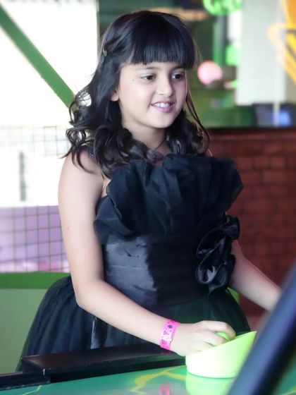 A candid shot of a young girl in a stylish black party dress, enjoying herself at an arcade. We capture kids' personalities in their element.
