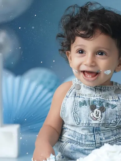 A close-up portrait capturing the infectious, frosting-filled smile of a baby boy during his first birthday cake smash.
