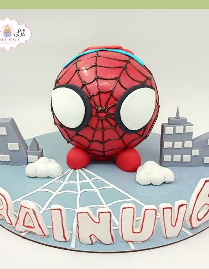A cute and spherical Spider-Man cake for Rainuv's 6th birthday, set against a mini city skyline.