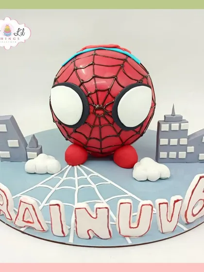 A cute and spherical Spider-Man cake for Rainuv's 6th birthday, set against a mini city skyline.