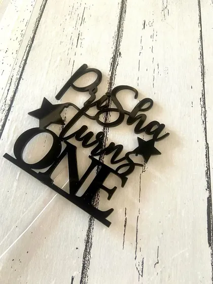 A flat-lay of the "Prisha turns ONE" topper, showing the clean edges and quality of the acrylic cut.