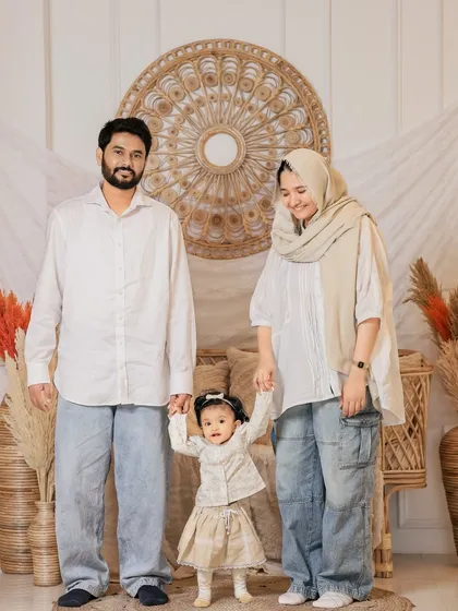 Capturing a baby's first steps is a precious milestone. Here, parents proudly hold their daughter's hands as she stands, all within the warm and stylish frame of our boho studio setup.