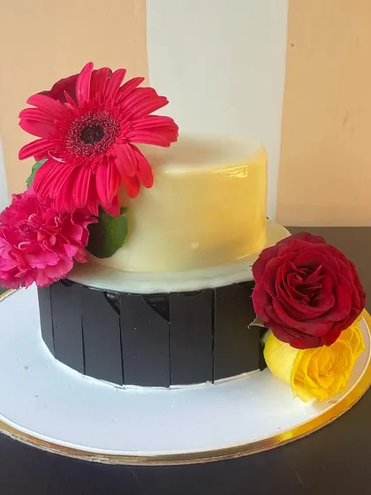 This angle highlights the modern, clean lines of the two-tier cake, where the dark chocolate panels meet the glossy white ganache, complemented by the softness of the fresh flowers.