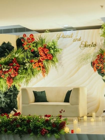 A modern and elegant reception stage with a striking floral installation. The blend of deep greens and vibrant reds against a clean, structured backdrop creates a sophisticated look.