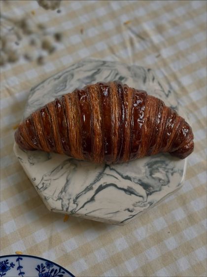 A shiny, perfectly laminated chocolate croissant, showcasing the beautiful layers of butter and dough that make our viennoiserie so special.