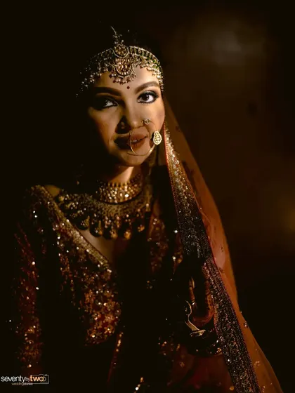 A bride's face is illuminated in the dark, her traditional jewelry and features highlighted in a play of light and shadow. A powerful and dramatic portrait.