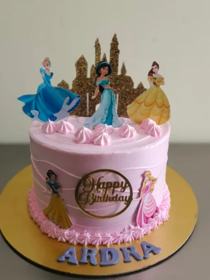 A pretty pink princess theme cake featuring Cinderella, Jasmine, and Belle, complete with a glittering gold castle topper.