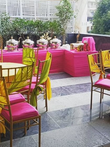 A vibrant and colorful setup for a pooja event at La Lagune, Gurgaon. The bright pink and yellow theme creates a cheerful and festive atmosphere.