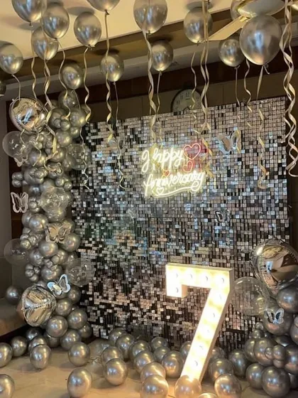 A glamorous 7th-anniversary setup featuring an all-silver theme with a sparkling shimmer wall. The design includes a neon sign, marquee number, and chrome balloons for a truly dazzling effect.