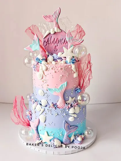 A fabulous two-tier mermaid cake in pastel perfection. This design for a fifth birthday features an ombre of pink, purple, and blue, decorated with shimmering mermaid tails, seashells, and magical bubbles.