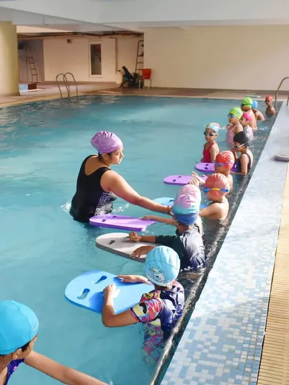 I believe in hands-on coaching, especially for young beginners. Here, our female coach guides kids through their first kicking exercises with kickboards in our Gurgaon pool.