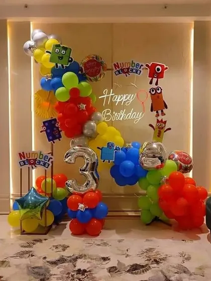 A colorful and educational Numberblocks theme for a 3rd birthday. The setup includes character cutouts, a "Happy Birthday" neon sign, and a primary color balloon arrangement.
