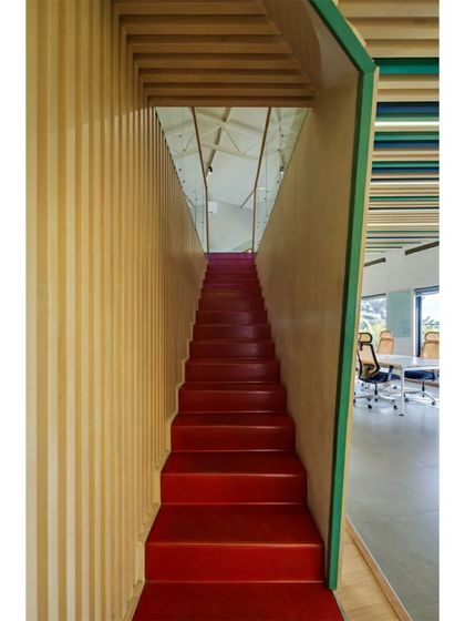 The vibrant red staircase of the Kadence Office provides a stark, colorful contrast to the surrounding wood-slatted walls. This architectural intervention serves as a central, energetic link between the office's two levels.