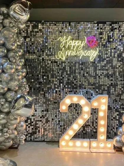 A glamorous 21st anniversary celebration with a silver sequin wall, a silver balloon arrangement, and large light-up numbers.